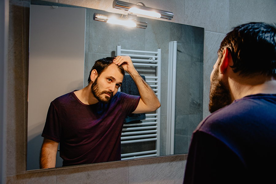 A worried young white man looks at himself in the mirror and ins