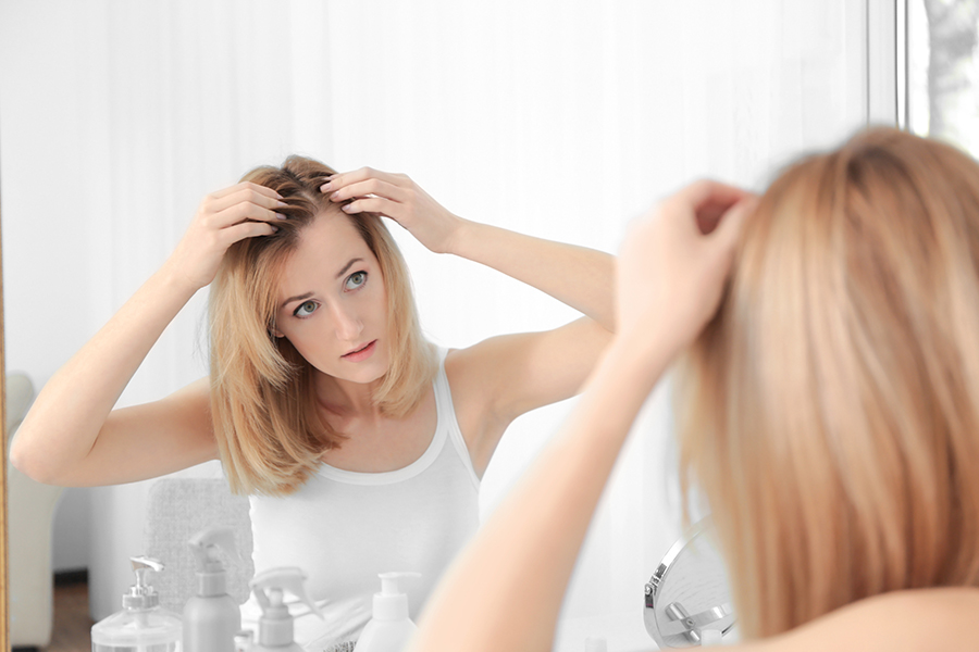 Young woman with hair loss problem looking in mirror at home